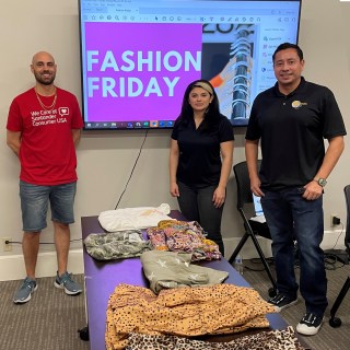 Three volunteers working a clothing drive and standing in front of a screen that says Fashion Friday.