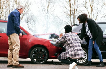 Three people examining two cars that have been in a head on accident.