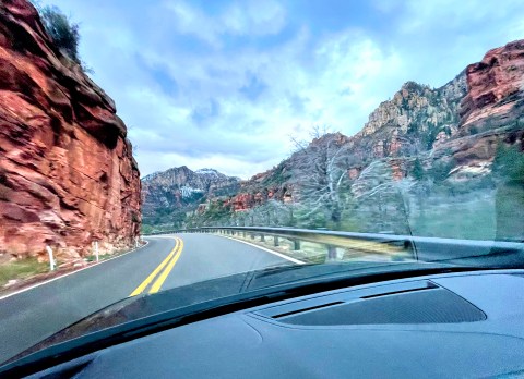 Looking out the front windshield of a car at cliffs along the road.