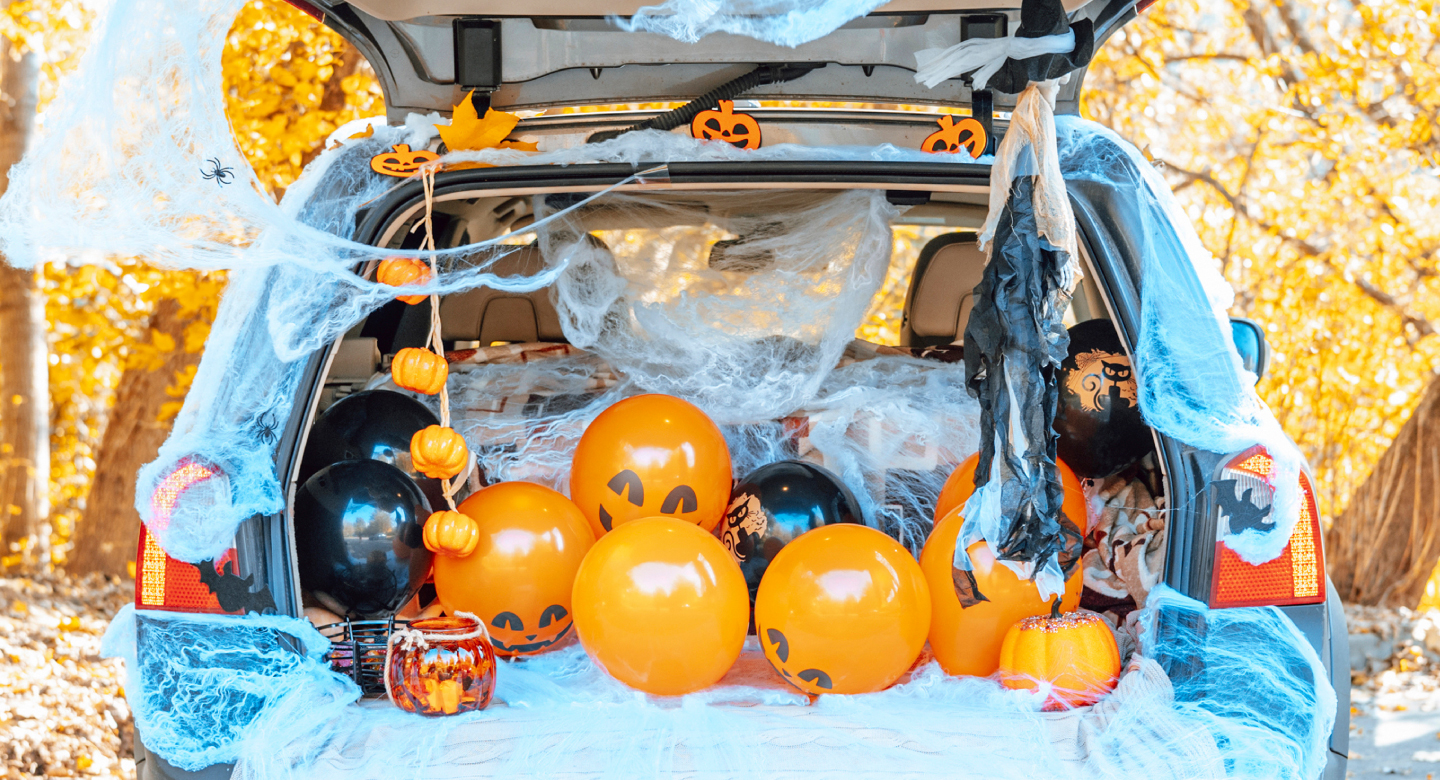 Open trunk of a car filled with Halloween decorations including balloons, cobwebs and pumpkins.