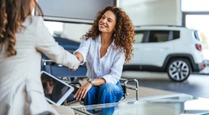 Woman at a car dealership shaking hands with a woman holding a tablet computer.