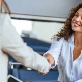 Woman at a car dealership shaking hands with a woman holding a tablet computer.