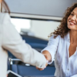 Woman at a car dealership shaking hands with a woman holding a tablet computer.